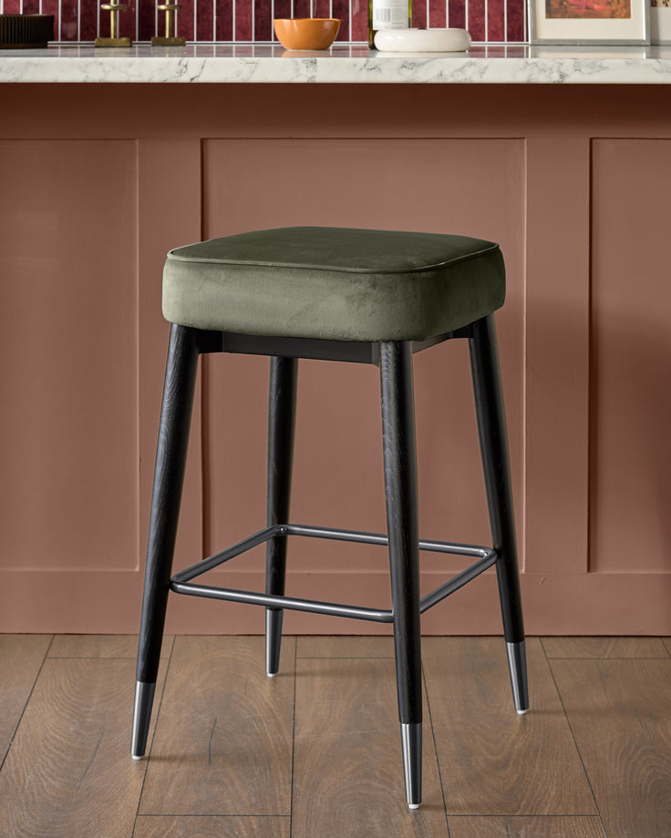 Clover velvet backless bar stool in olive green with dark wood legs and metal footrest.