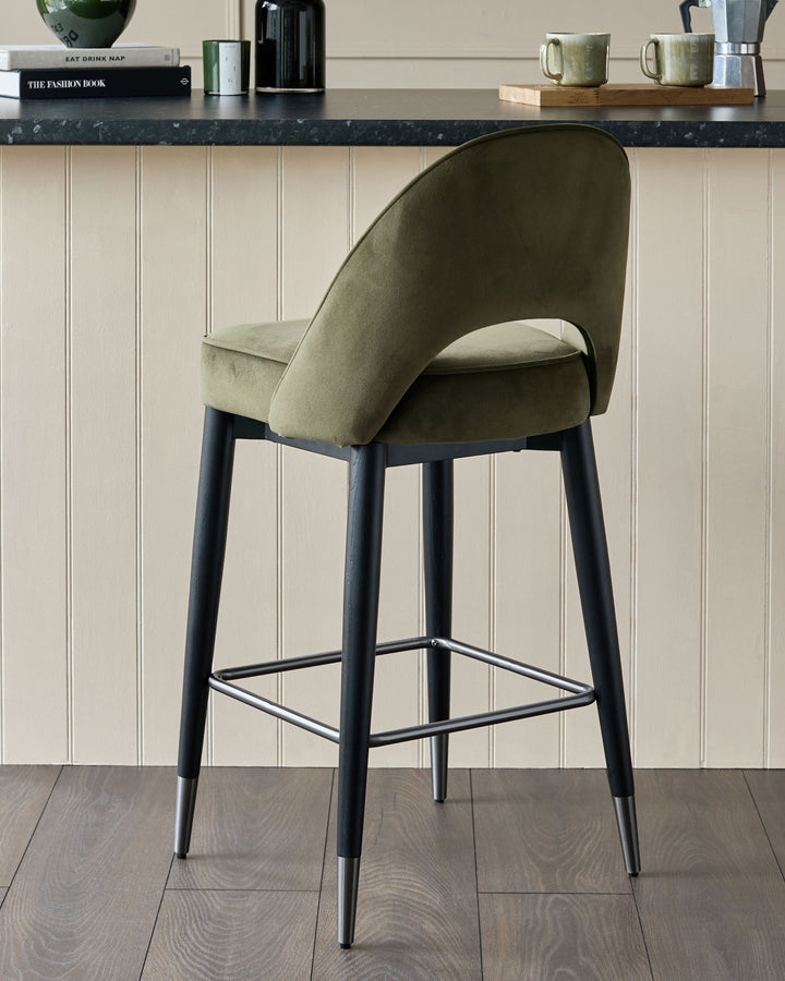 Olive green velvet bar stool with a black frame and silver accents.