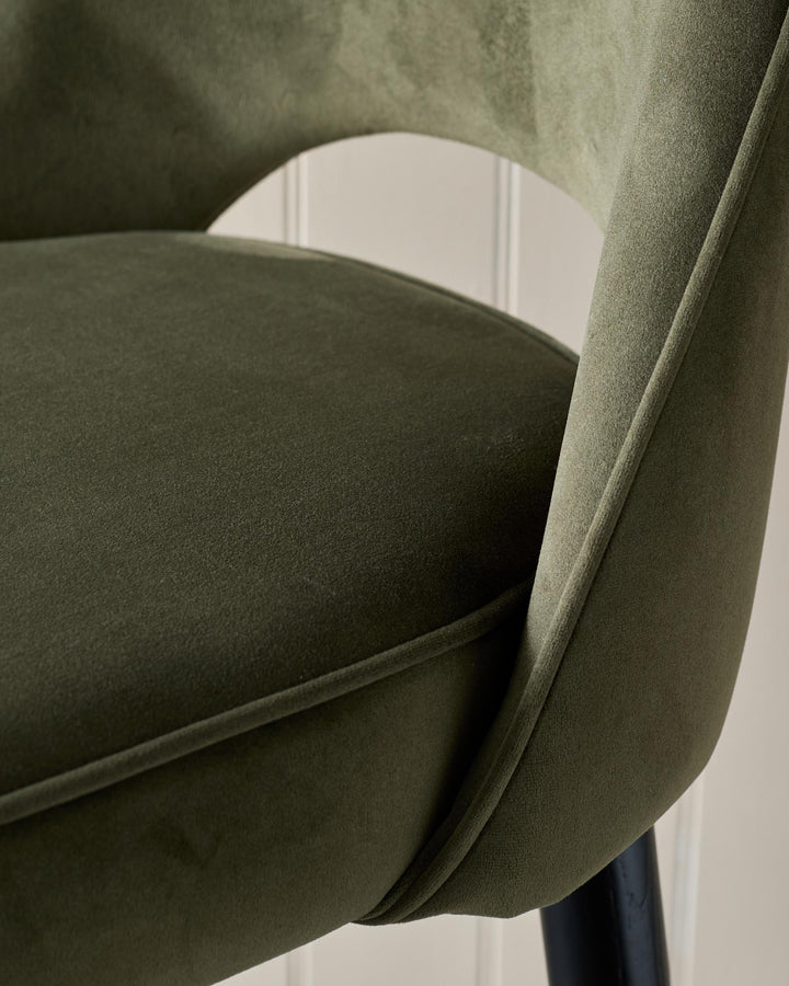 Close-up of a stylish, olive-green velvet chair with a curved back, showcasing its texture and design.