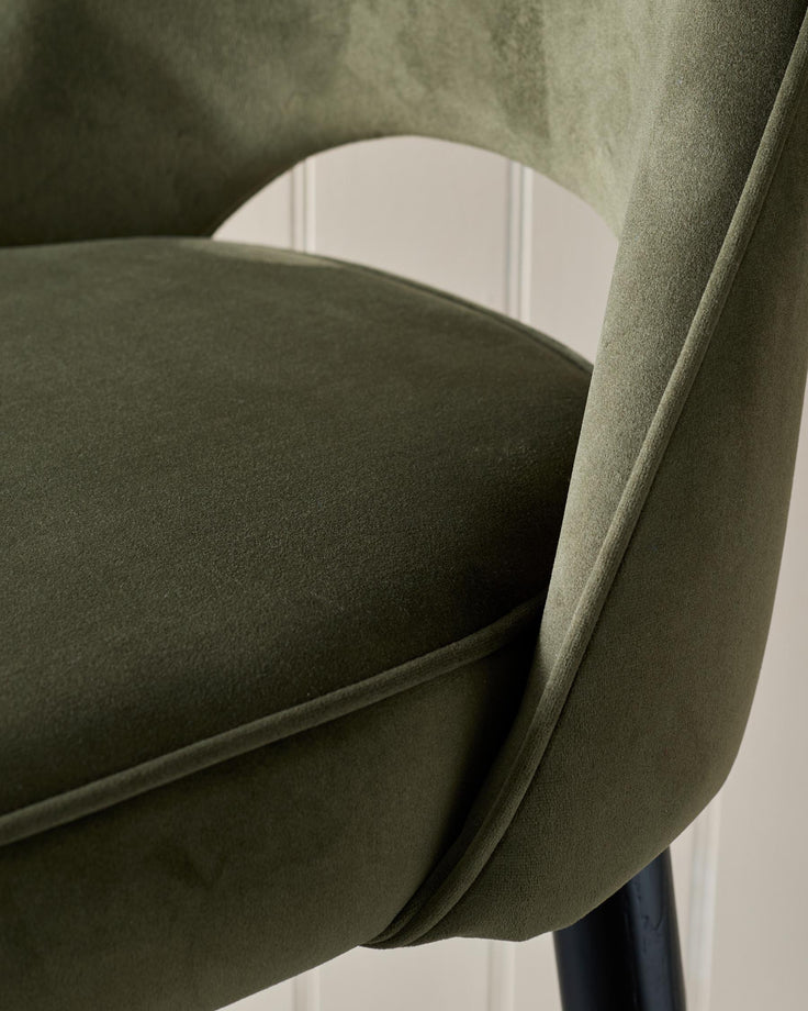 Close-up of a stylish, olive-green velvet chair with a curved back, showcasing its texture and design.