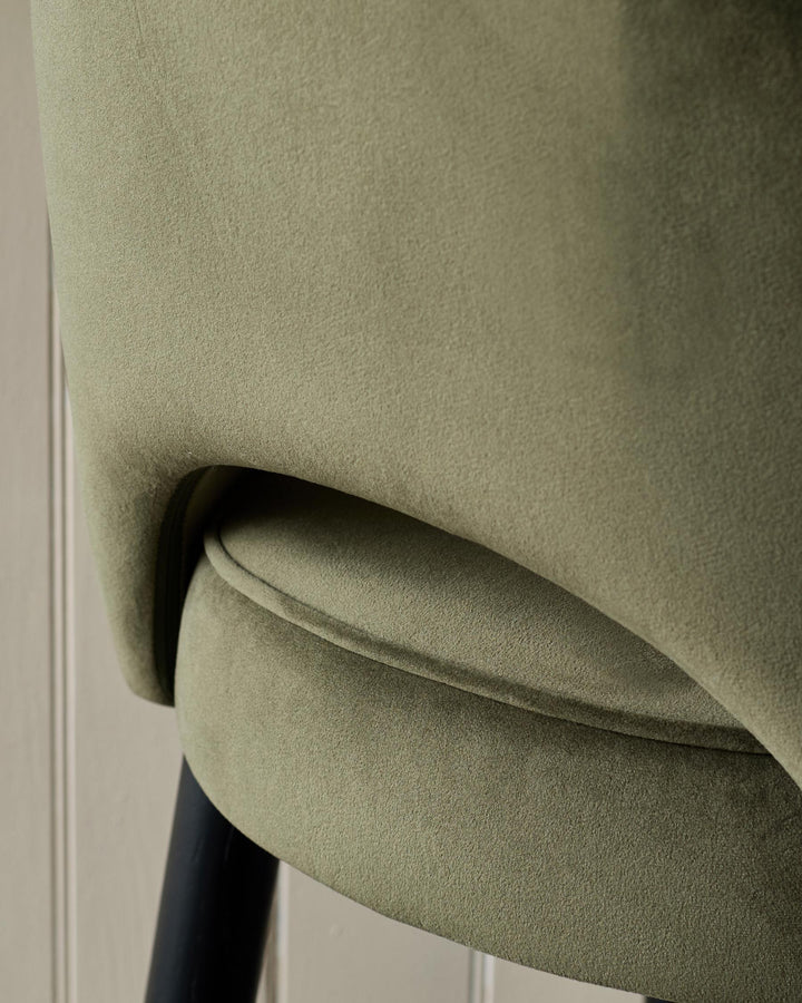 Close-up of a stylish olive green velvet chair with black legs, showcasing its texture and design details.