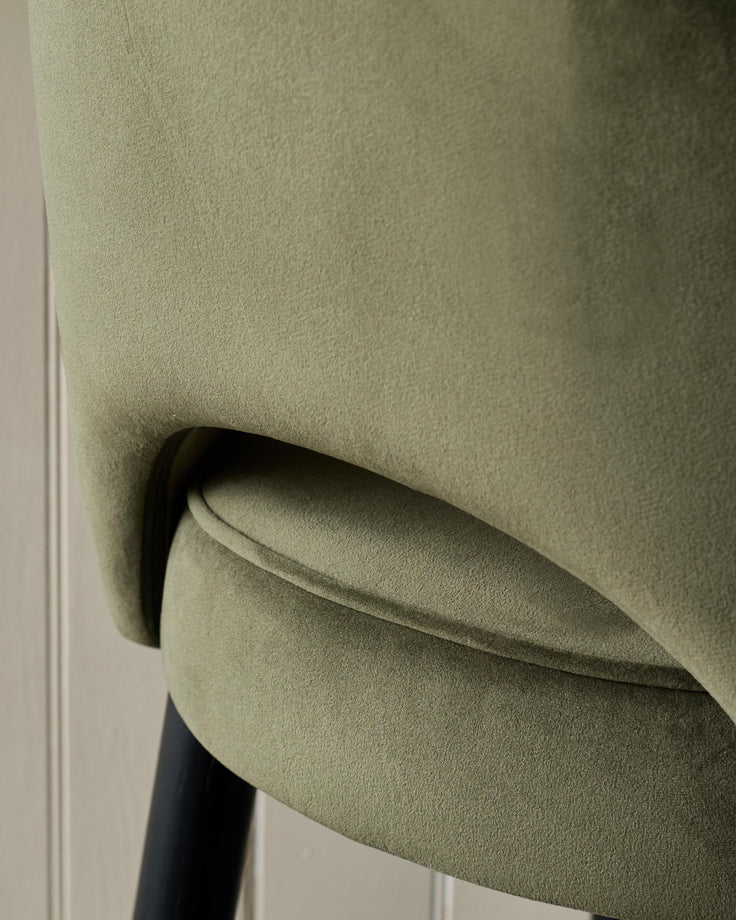 Close-up of a stylish olive green velvet chair with black legs, showcasing its texture and design details.