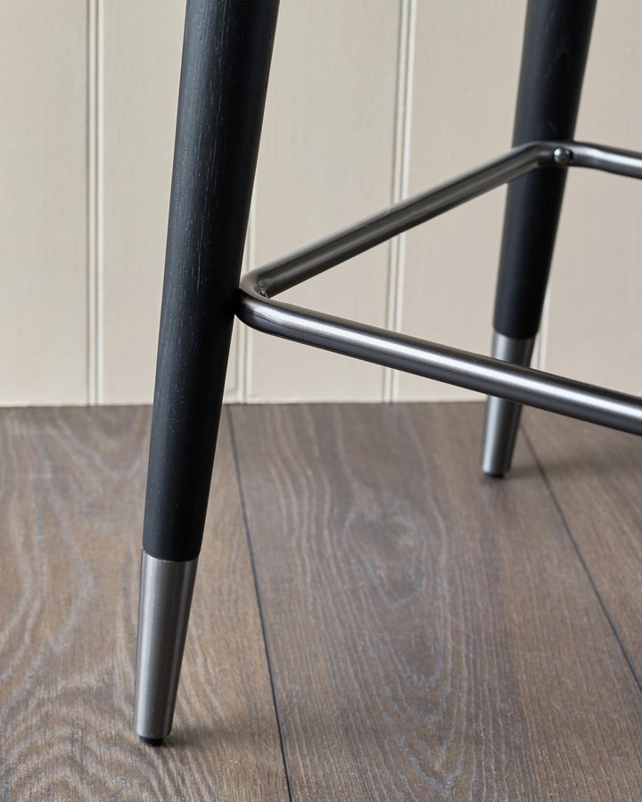 Close-up of a stylish bar stool with black wooden legs and silver footrest, showcasing modern furniture design.