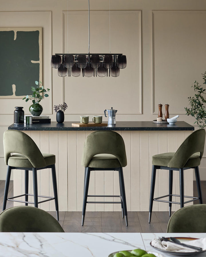 Olive green bar stools at a kitchen island with a black countertop and modern lighting fixture.
