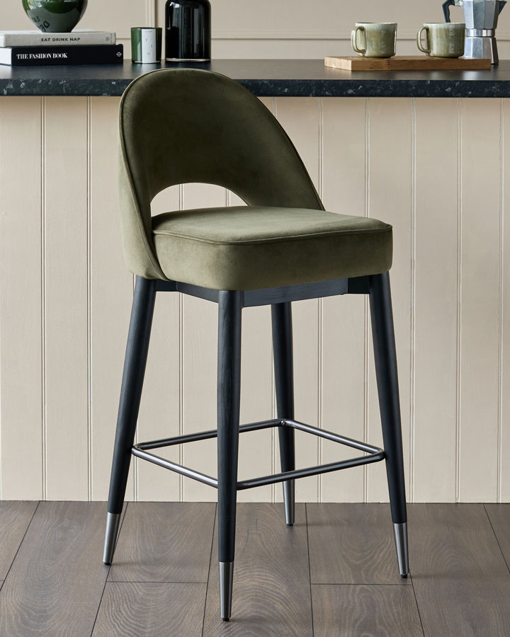 Olive green velvet bar stool with dark wooden legs and silver foot rest.
