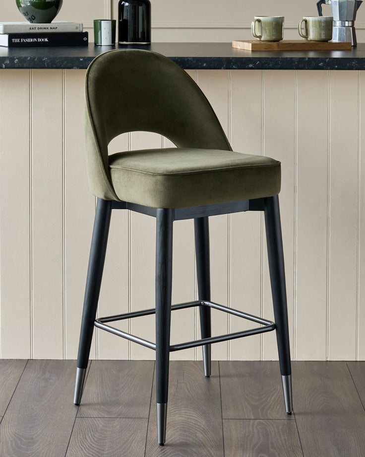 Olive green velvet bar stool with dark wooden legs and silver foot rest.