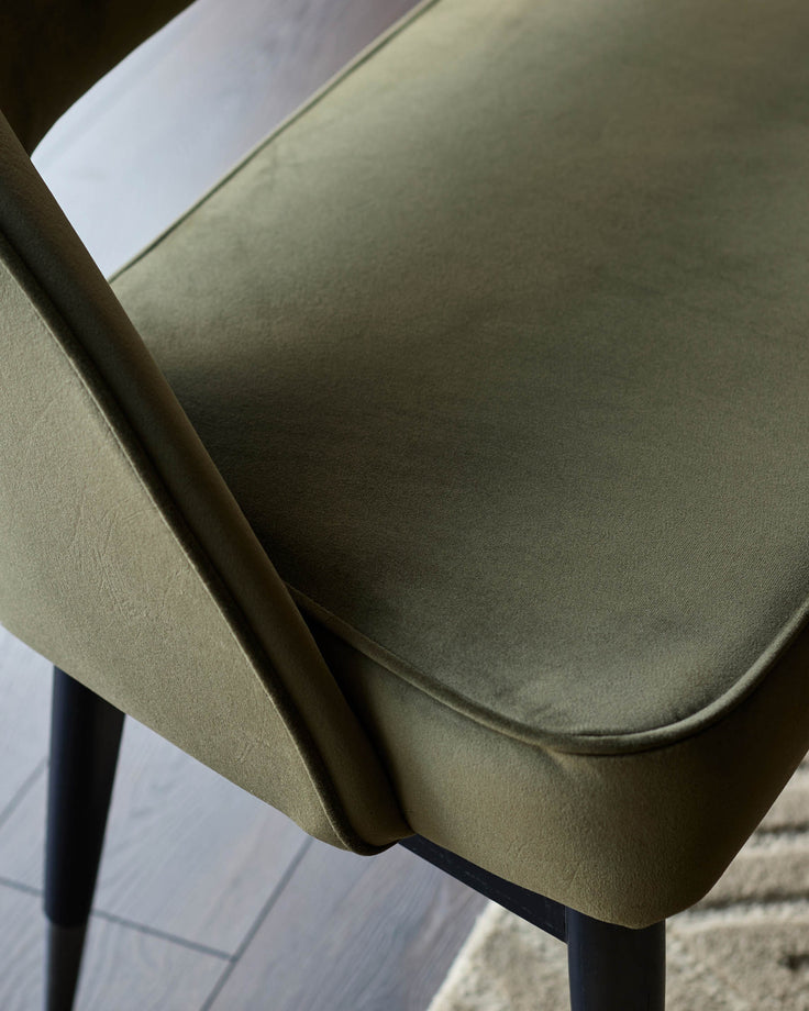 Close-up of a modern green velvet chair with black legs, showcasing its plush texture and design details.