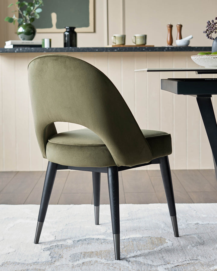An olive green velvet chair with black wooden legs & silver caps. An elegant addition to any modern dining room.