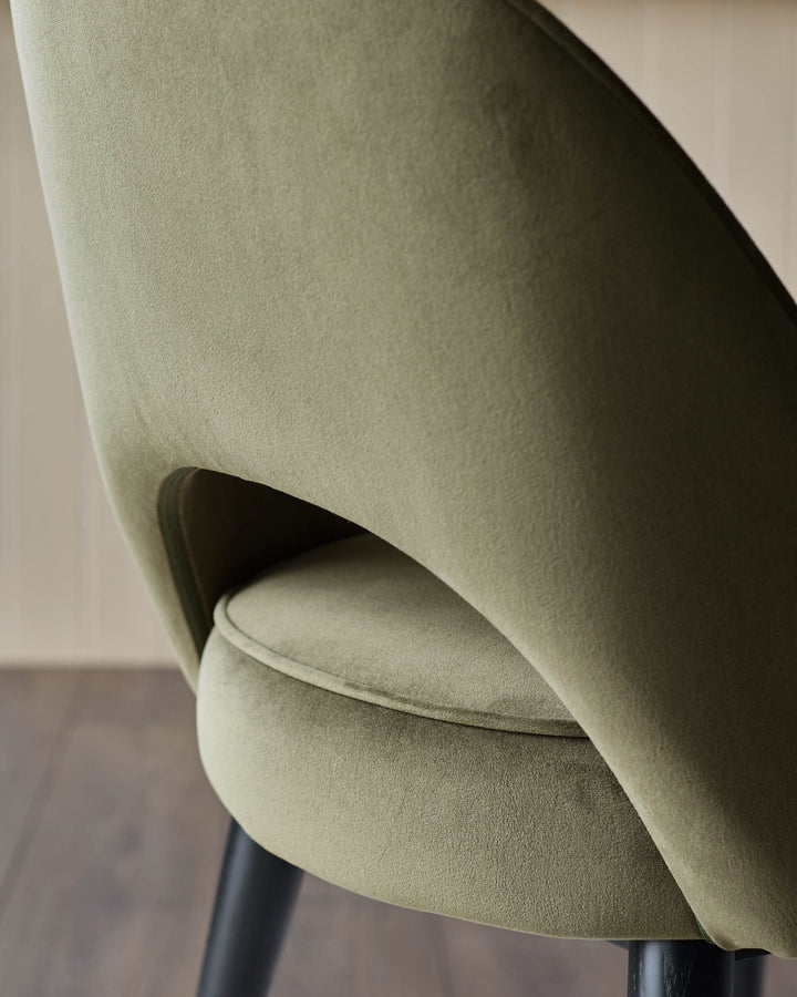 Close-up of a stylish olive-green velvet chair, showcasing its curved design and plush texture. Modern elegance for any room.