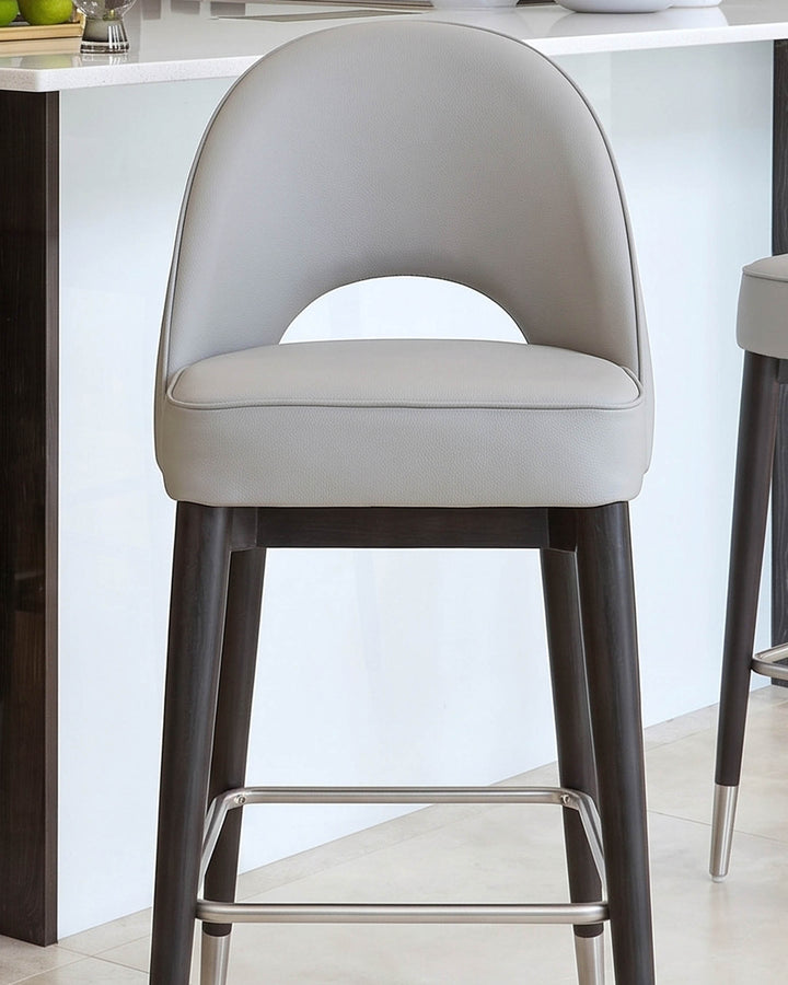 Light grey faux leather bar stool with curved backrest and dark wood legs with metal footrest.