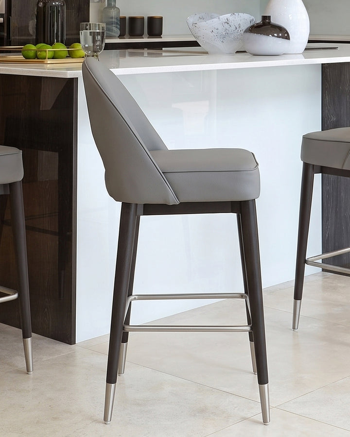 Clover mid-grey faux leather bar stool with dark wood legs and metal footrest, positioned at white kitchen island.