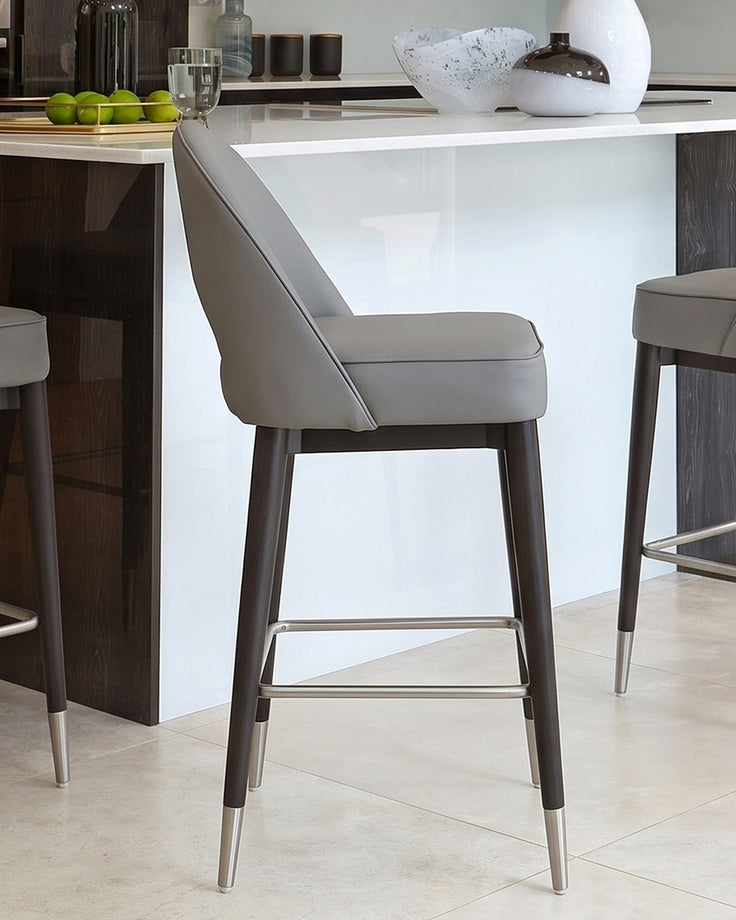 Clover mid-grey faux leather bar stool with dark wood legs and metal footrest, positioned at white kitchen island.