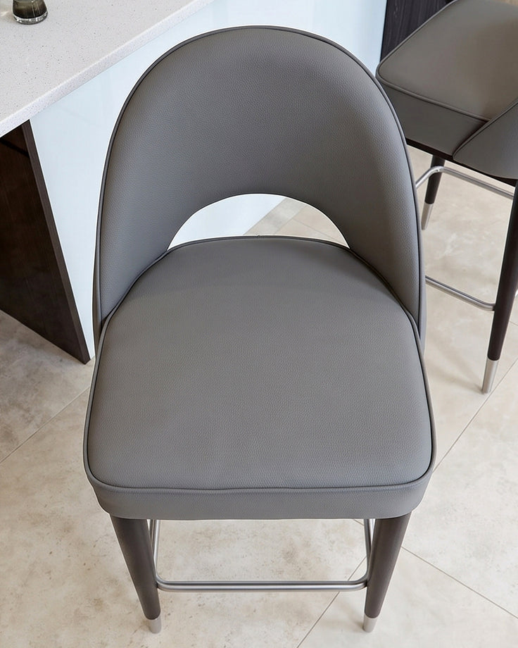Clover mid-grey faux-leather bar stool with curved backrest, viewed from front, showing padded seat and dark legs.