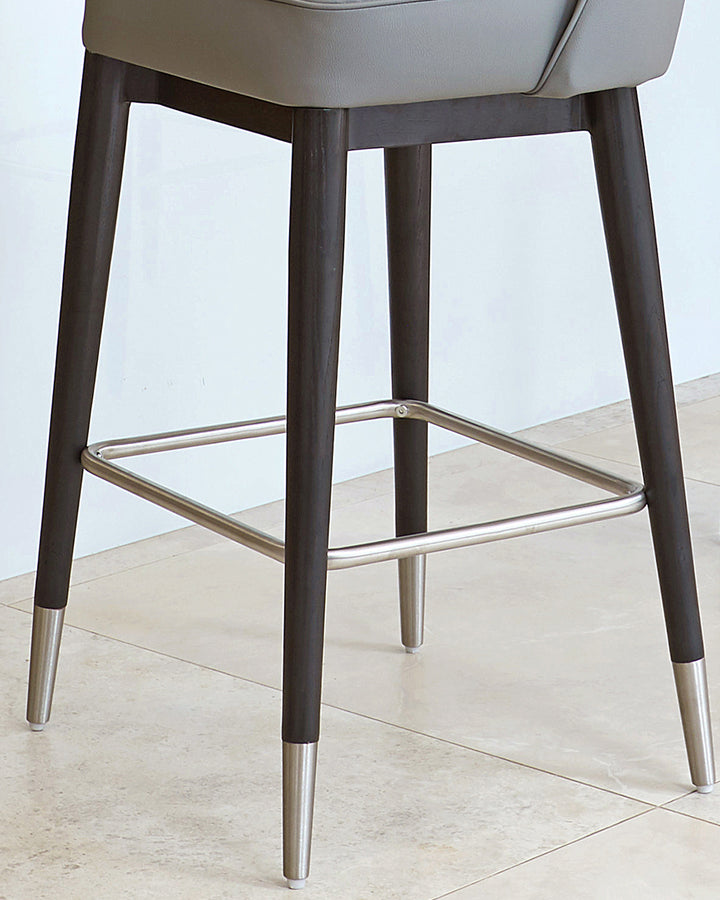 Clover faux-leather bar stool in mid-grey with dark wood legs, metal footrest, and brushed metal foot caps.