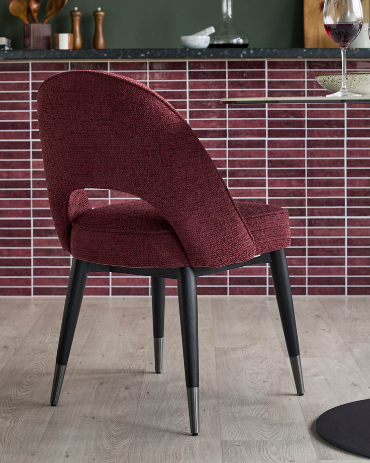 A stylish, maroon upholstered dining chair with sleek, black legs and metal accents. Perfect for modern dining spaces.
