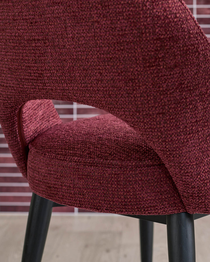 Close up of a modern chair in a textured dark red fabric with black legs.