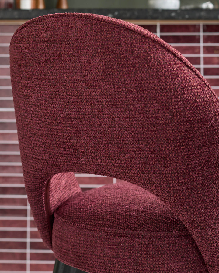 Close-up of a stylish burgundy fabric chair, showing its textured upholstery and curved back design against a tiled wall.