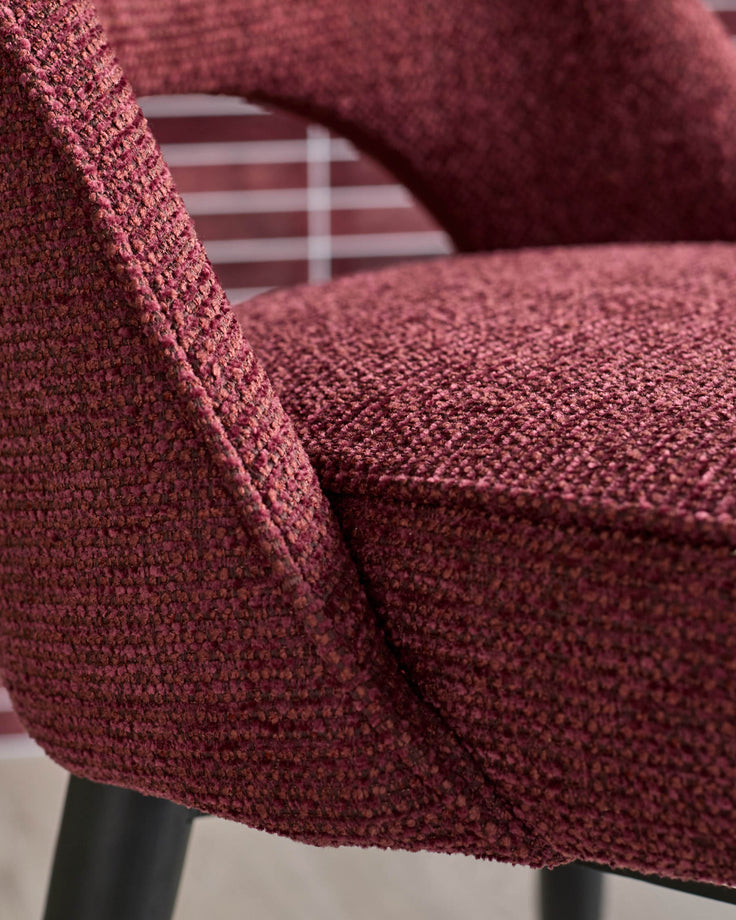 Close-up of a stylish, textured burgundy chair showing its armrest and seat, exuding comfort and modern design.