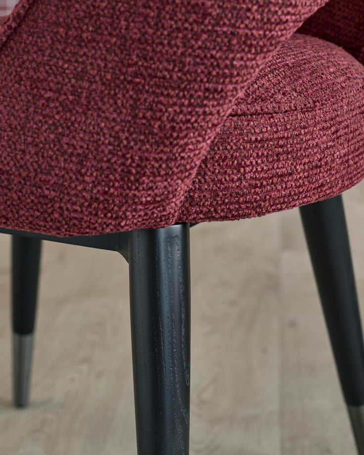 Close-up of a stylish red upholstered chair with sleek black legs, showcasing its modern design.