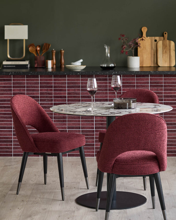 A dining area with round marble table surrounded by stylish red chairs with dark legs and silver details.