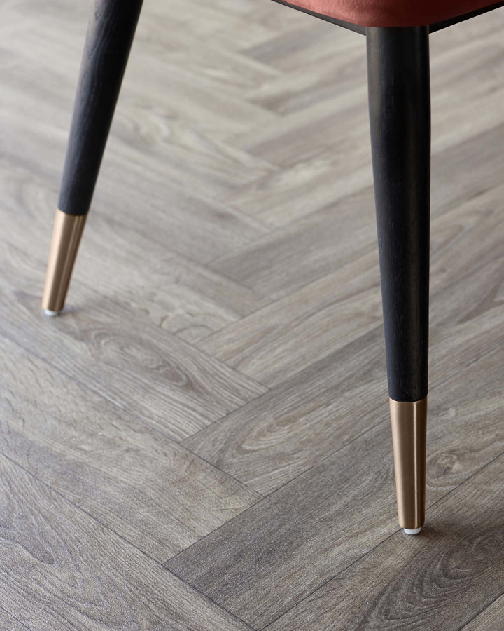 Close up of a chair leg with brass foot, on a herringbone grey wood floor. Shows attention to detail and luxury materials.