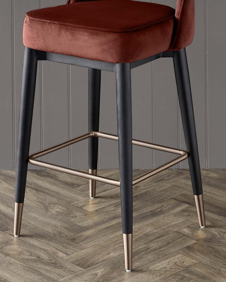 Close-up of a stylish bar stool with dark wood legs, copper accents and a rust-coloured, velvet seat.