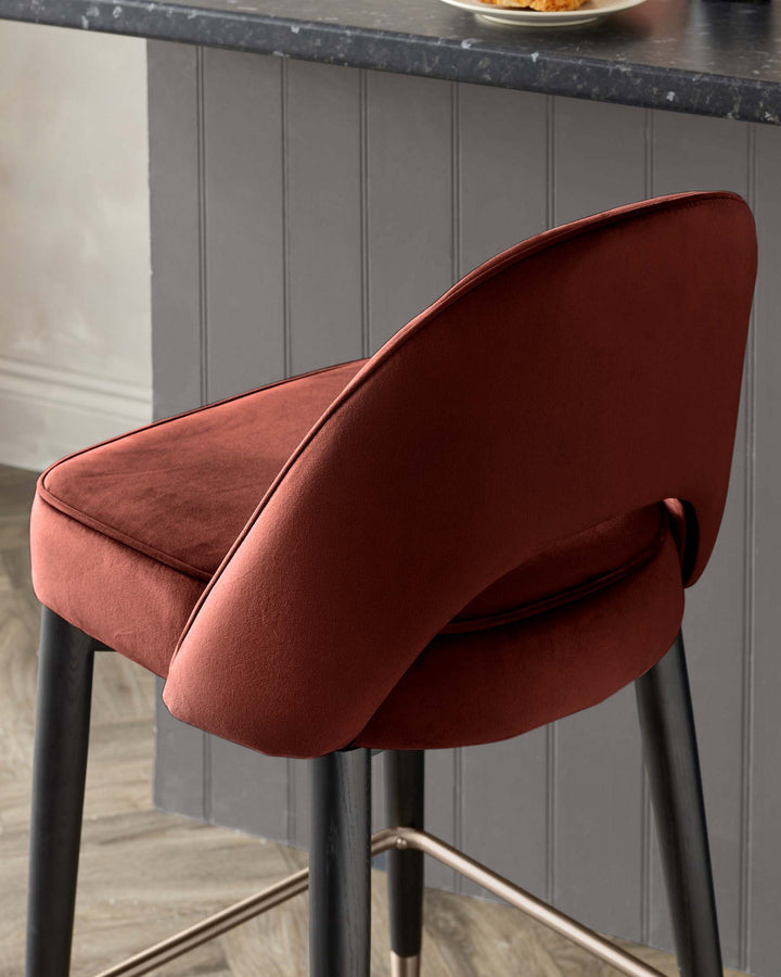 Close-up of a modern, velvet bar stool in a warm terracotta colour with a dark wood frame and brass footrest.