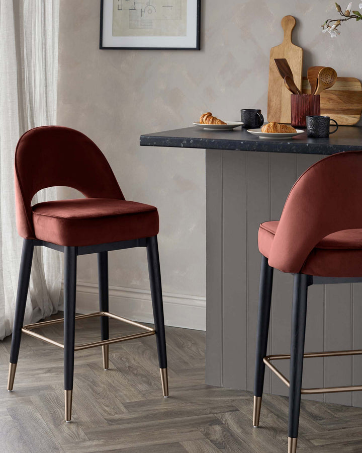 Two stylish, red velvet bar stools with black legs and metallic footrests sit at a dark grey breakfast bar.