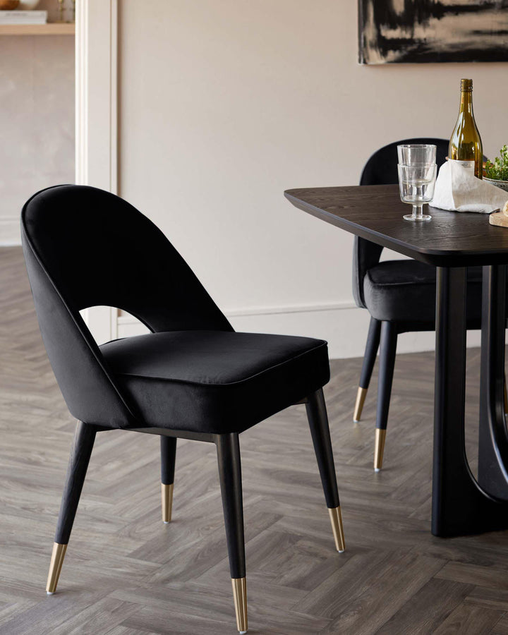 A black dining table with two chairs. The chairs have a velvet seat and back, and gold accents on the legs.