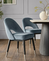 Clover blue velvet dining chair with curved backrest and stainless steel leg caps, shown at table.