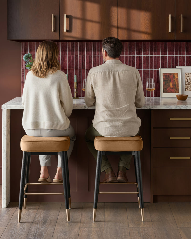 Caramel fabric backless bar stools with black legs and brass footrests, shown at kitchen counter.