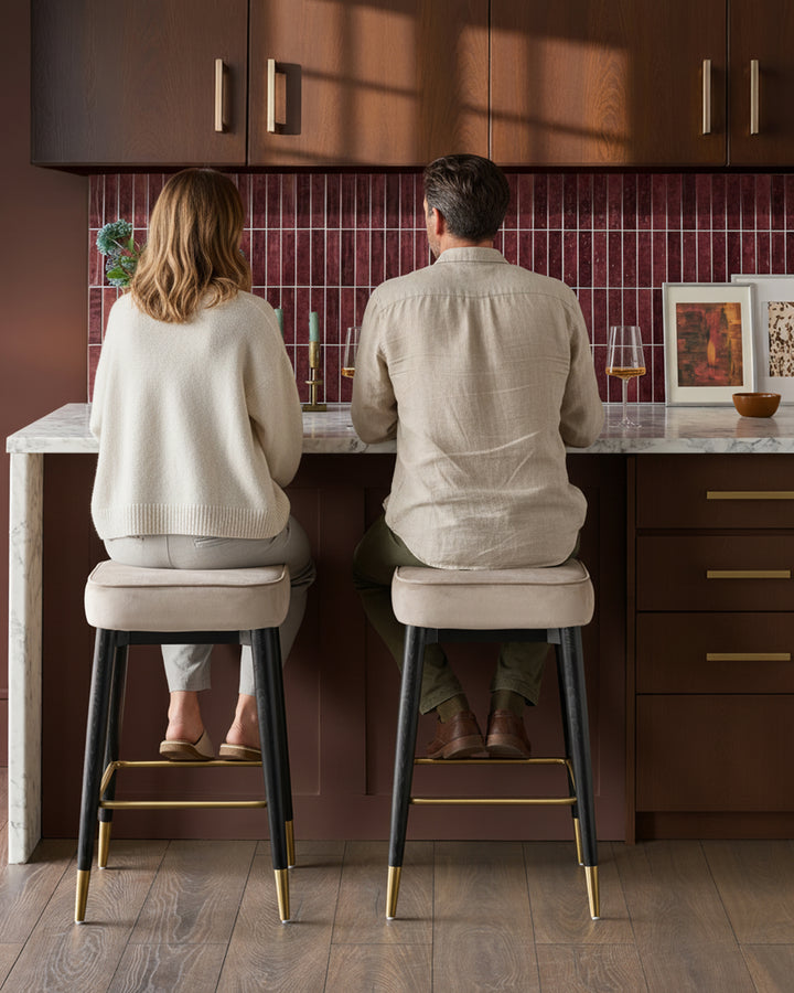 Champagne velvet backless bar stools with black legs and brass footrests, shown in a kitchen setting.