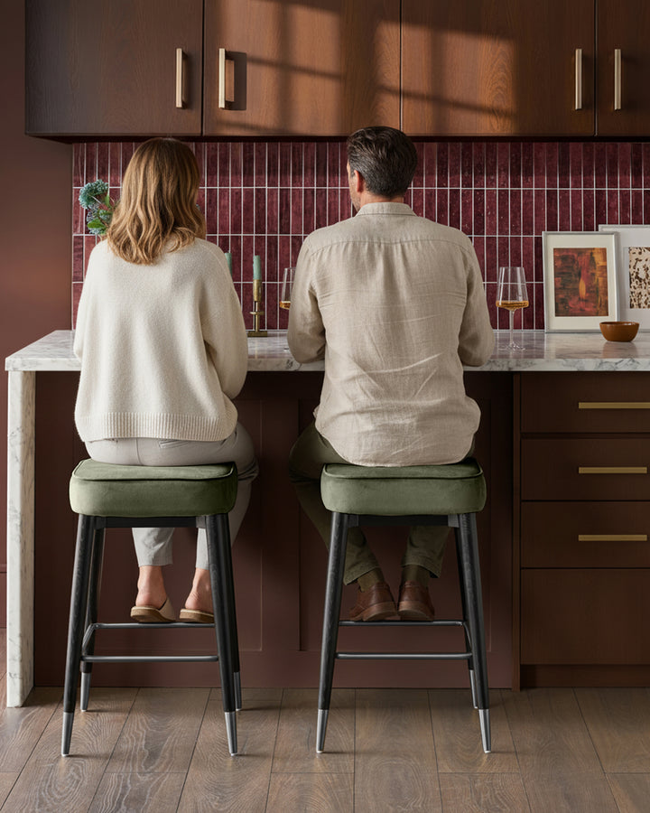 Clover velvet backless bar stools in olive green with black metal legs, shown as pair at kitchen counter.