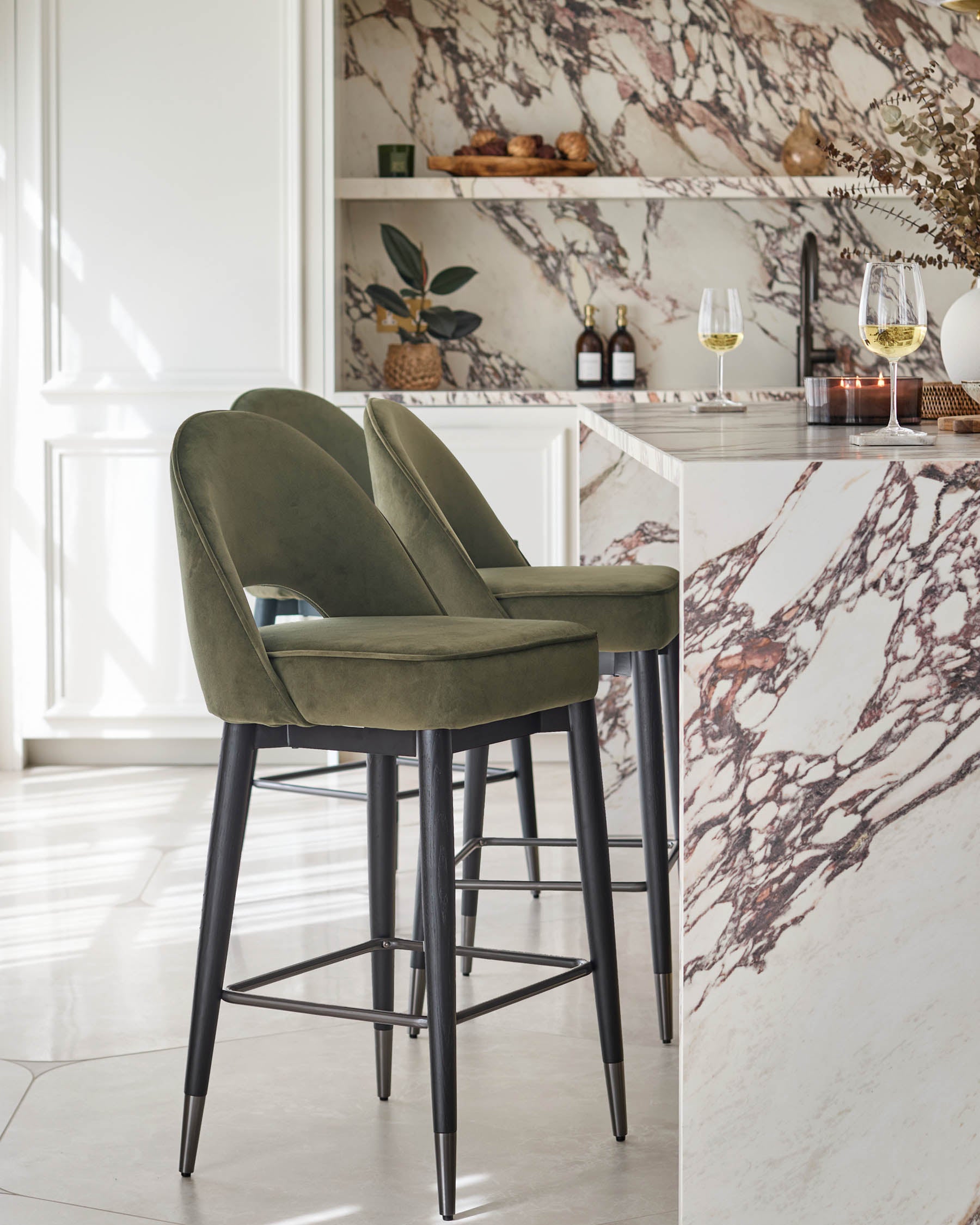 Two green velvet bar stools with black legs at a marble island. Modern design adds sophistication.