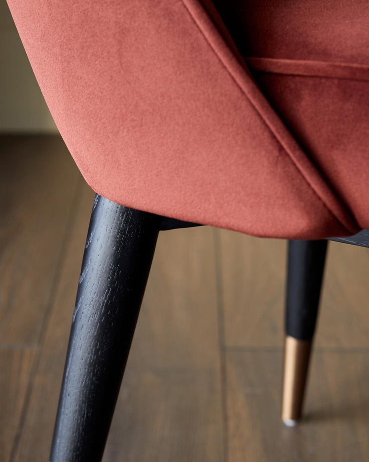Close-up of an upholstered armchair with sleek, dark wood legs and gold accents. Ideal for modern living spaces.