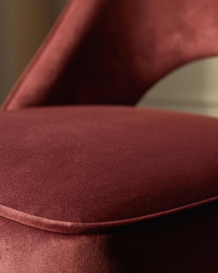 Close-up of a red velvet chair with a curved back, showcasing the texture and design of the seat.