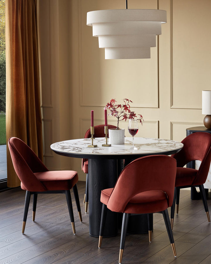 Round marble-topped dining table with statement chairs, set under a modern tiered light fixture. Perfect for elegant dining.