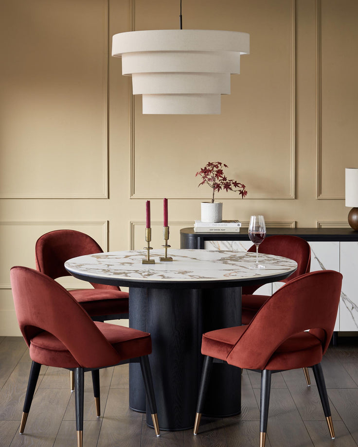 A stylish dining set featuring a round marble table, velvet chairs and a modern, tiered light fixture.