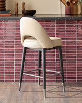 A modern beige bar stool with a curved back, dark wood legs and a stainless steel foot rest.