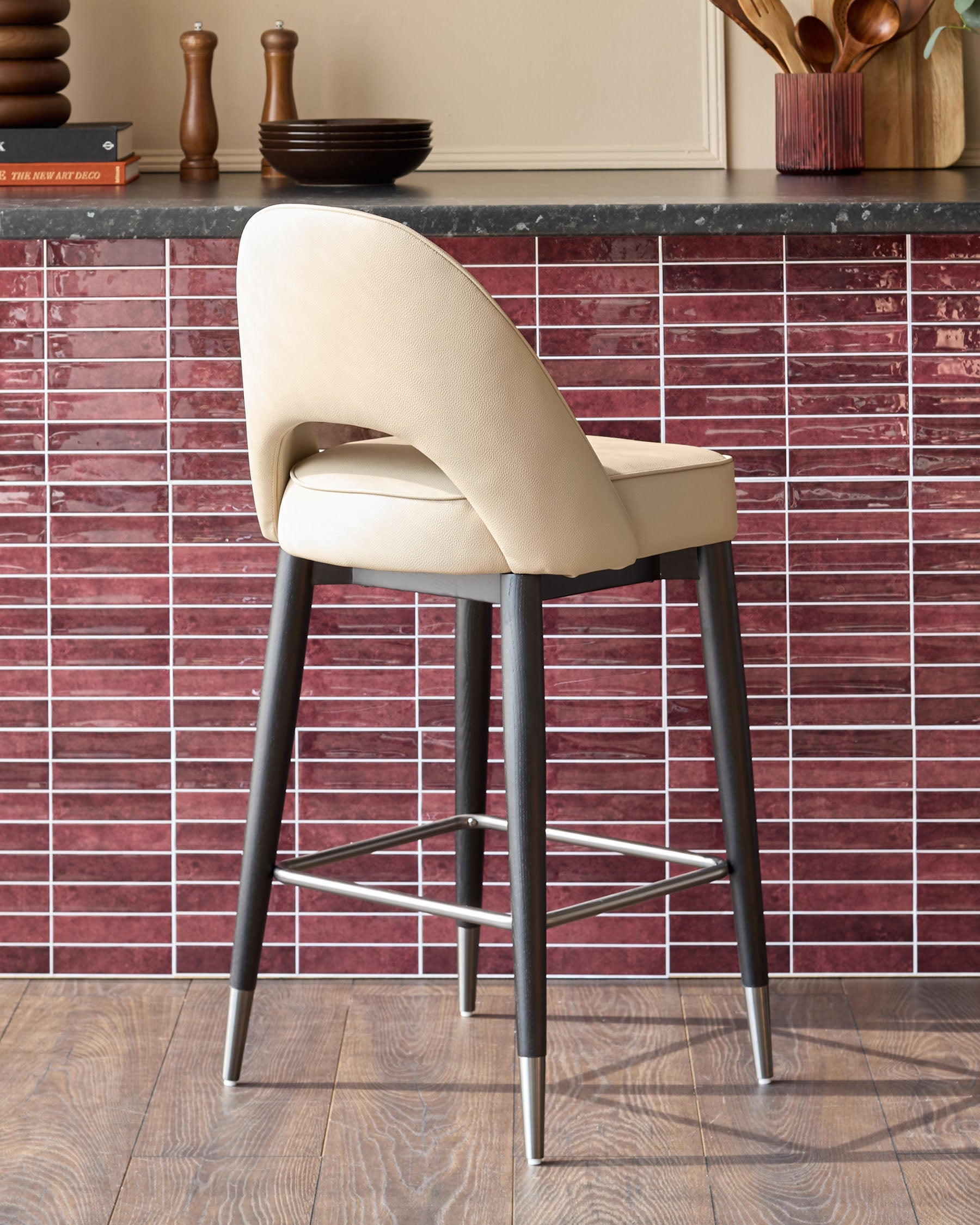 A modern beige bar stool with a curved back, dark wood legs and a stainless steel foot rest.