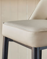 Close up of a light beige leather stool with dark wooden legs, showcasing its sleek design and quality materials.