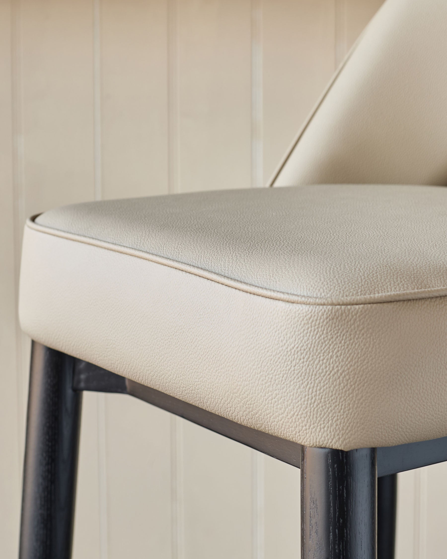 Close up of a light beige leather stool with dark wooden legs, showcasing its sleek design and quality materials.