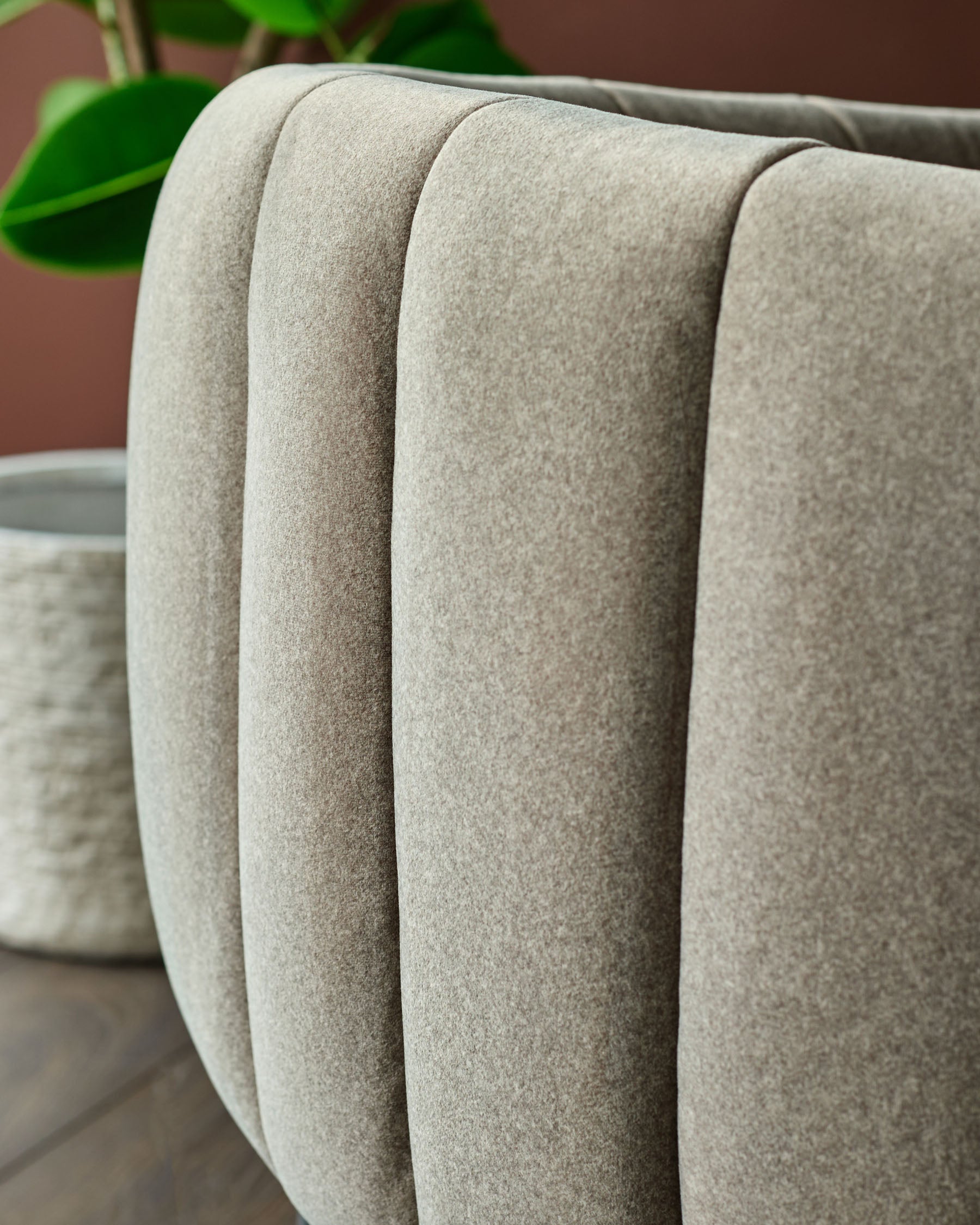 Close up of a ribbed, light brown, upholstered chair. Plant in the background.