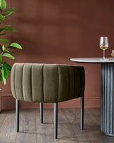 A contemporary ribbed stool in olive green with black legs, placed beside a round marble table with wine glasses on it.