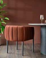 Stylish brown velvet chair beside a round table with a grey base and wine glass. Modern furniture for the dining room.