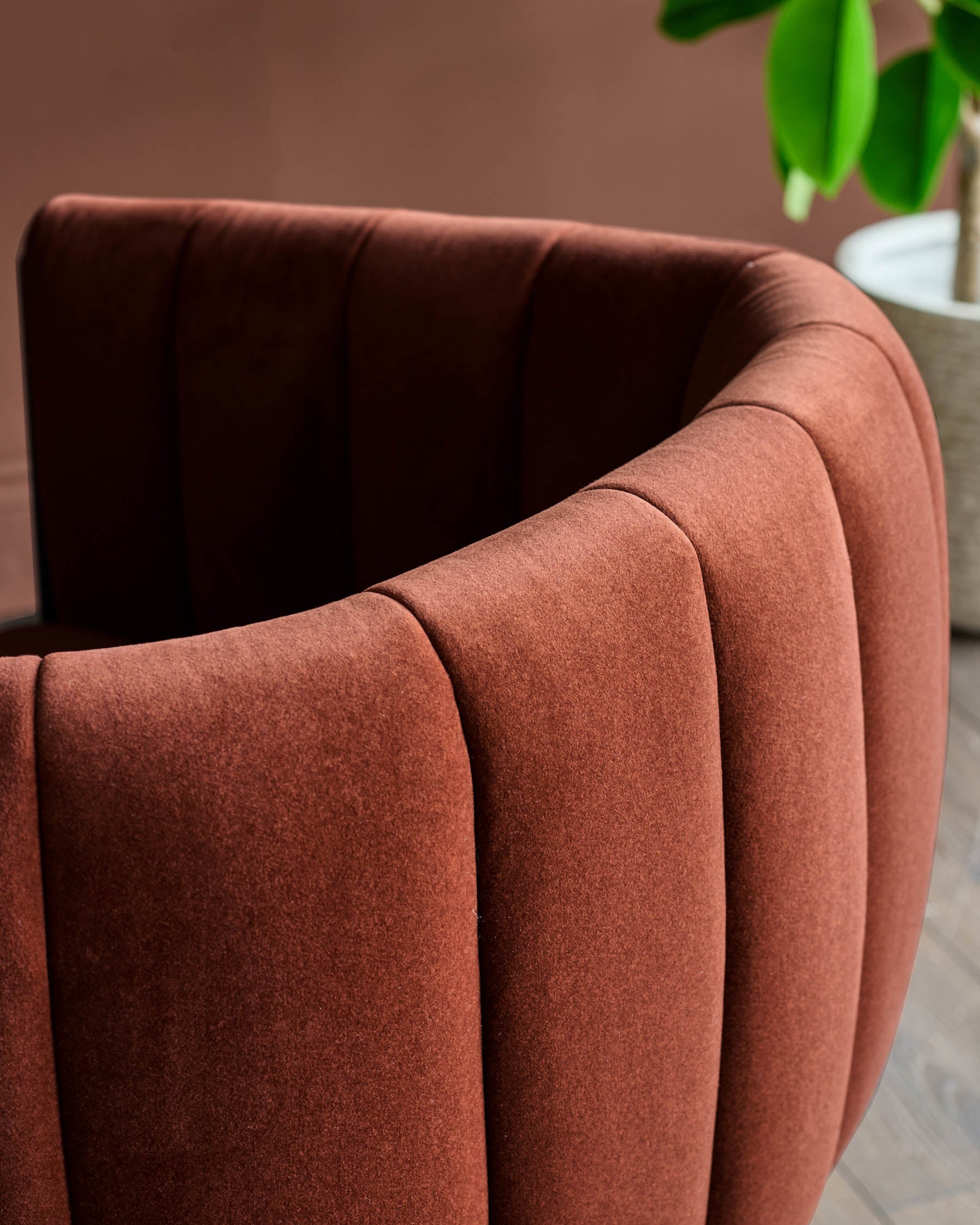 Close up of a stylish, curved, ribbed, maroon velvet chair with rounded back. Ideal accent furniture for modern homes.