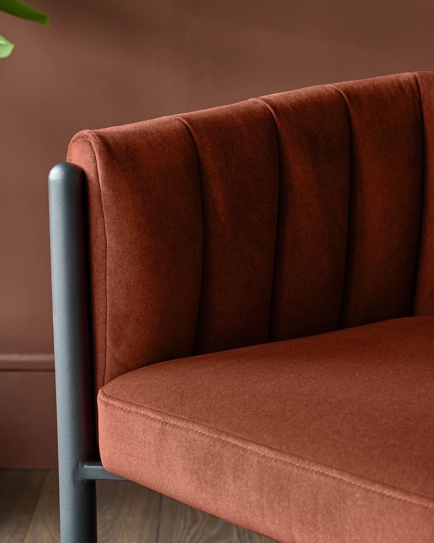 Close-up of a stylish, rust-coloured upholstered chair with a fluted back and matte black frame. Modern furniture detail.