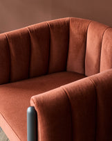 Close-up of a stylish, rust-coloured armchair with a channel-tufted back and grey arm.