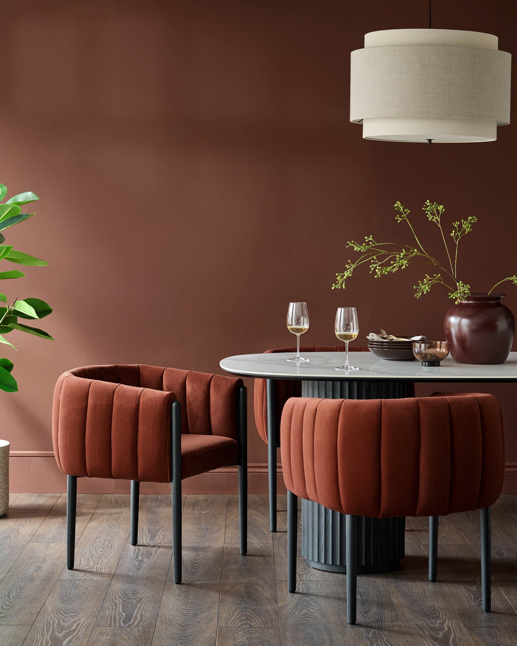 A dining set featuring a marble-top table and plush, rust-coloured dining chairs with sleek, dark grey legs.