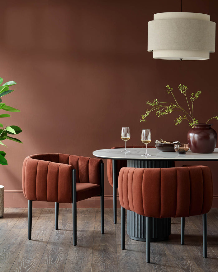 A dining set featuring a marble-top table and plush, rust-coloured dining chairs with sleek, dark grey legs.